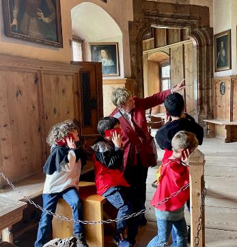 Kinderführung im Schloss Tratzberg mit einer Gruppe von Kindern, die aufmerksam einer Führungsperson zuhören und den historischen Raum erkunden.